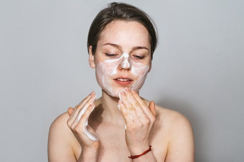 Front image of woman cleaning her face with exfoliant