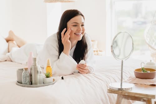 Woman lying on bed doing her skin care routine