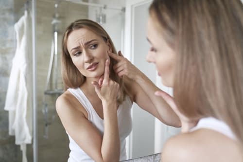 Woman with acne looking at mirror