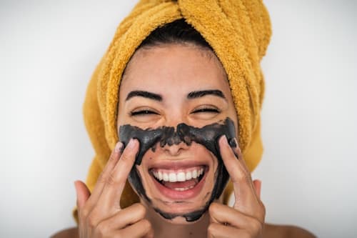 Happy woman washing her face with activated charcoal