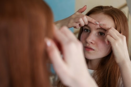 Young woman trying to pop her pimple