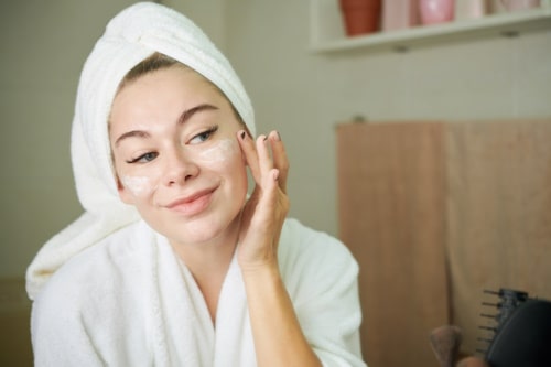 Woman with towel applying face cream