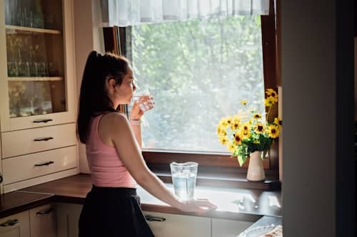 young woman drining water near window