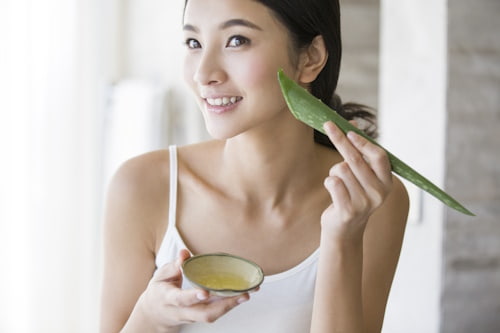 Asian woman applying aloea vera directly to her face