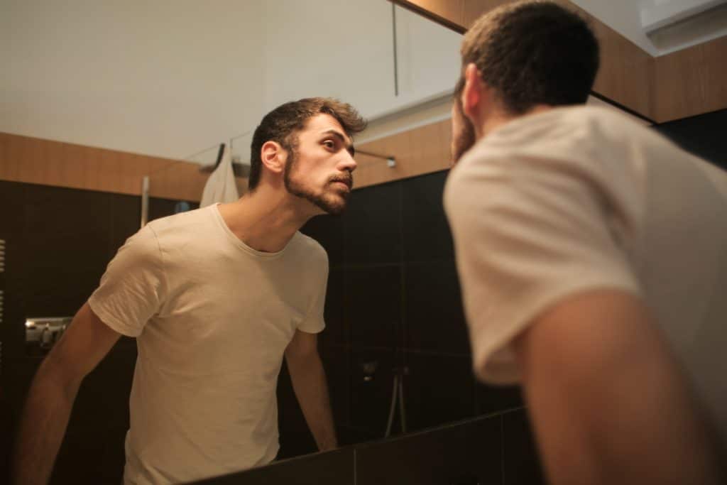 A man looking in the mirror and considering zinc for acne