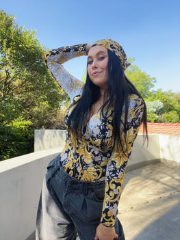 Side view of top, model is standing, wearing a matching fabric bandana, palm trees in the background.