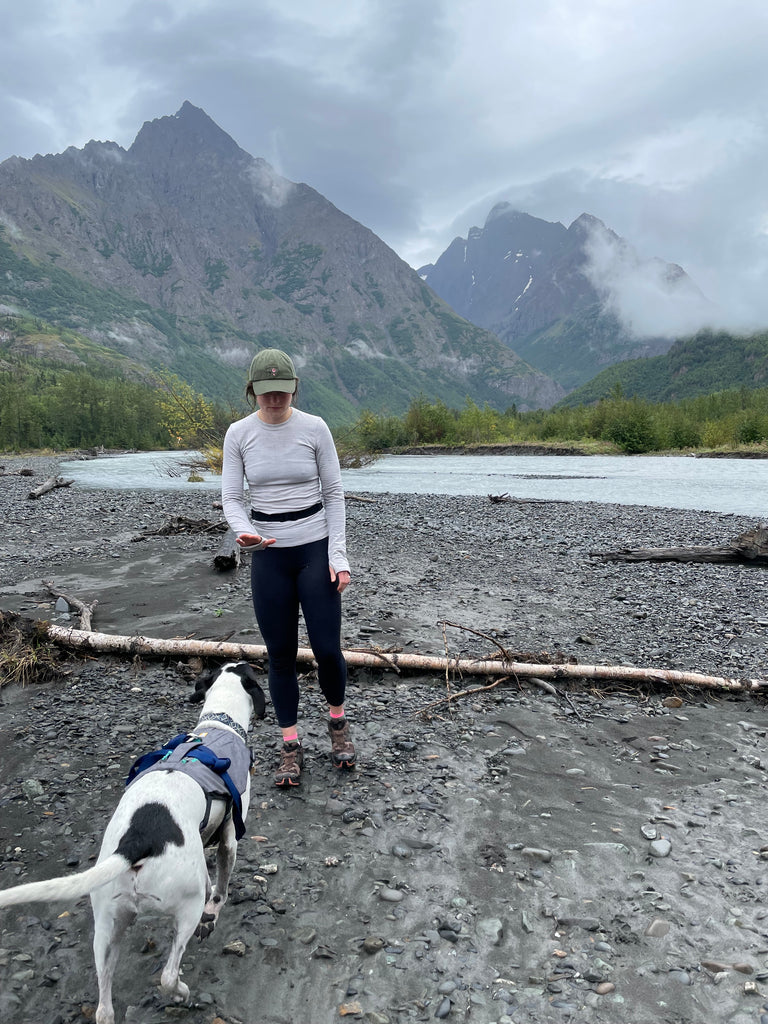 Woman with white and black dog on river bed with mountains in the background