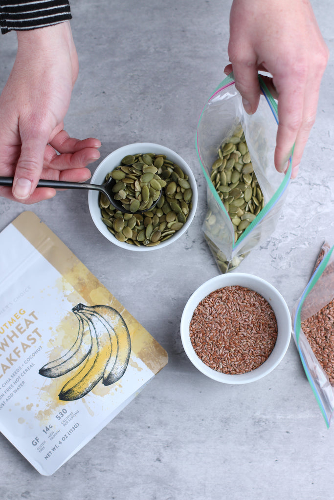 banana buckwheat breakfast next to bowl of flax seeds and hands scooping pumpkin seeds from small bowl into plastic bag