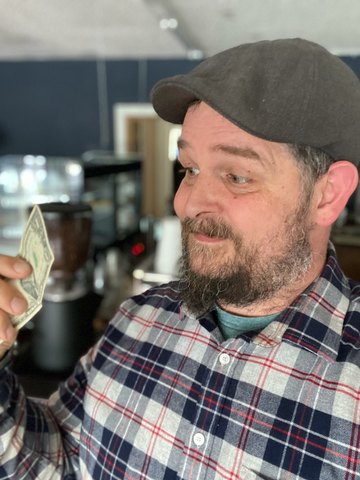Man looking at a dollar bill in from of espresso bar
