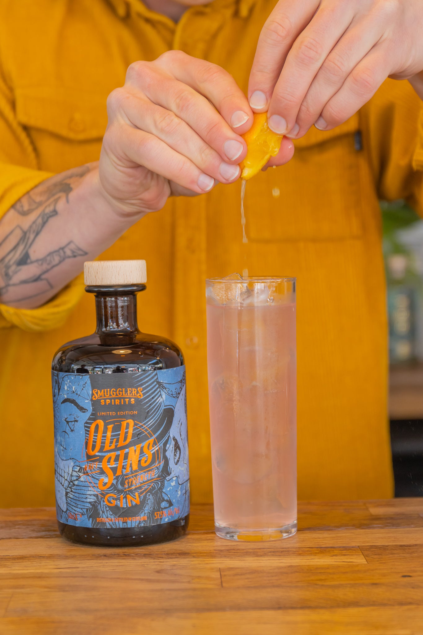 A pair of hands squeeze the juice of an orange wedge into a gin and ginger cocktail