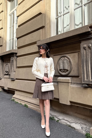 une dame en haut beige, une veste en tweed blanche et une jupe plissée en laine marron