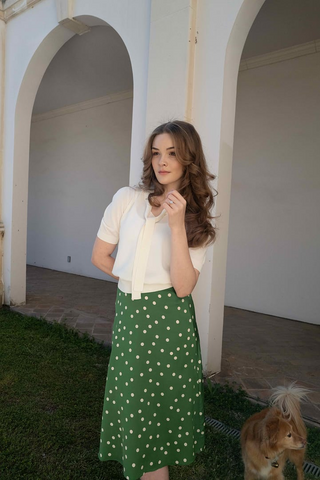 a lady in a white bow tie neck shirt and a green skirt with white polka sots