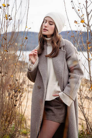 a lady in a beige sweater, a grey wool coat and a pair of brown shorts