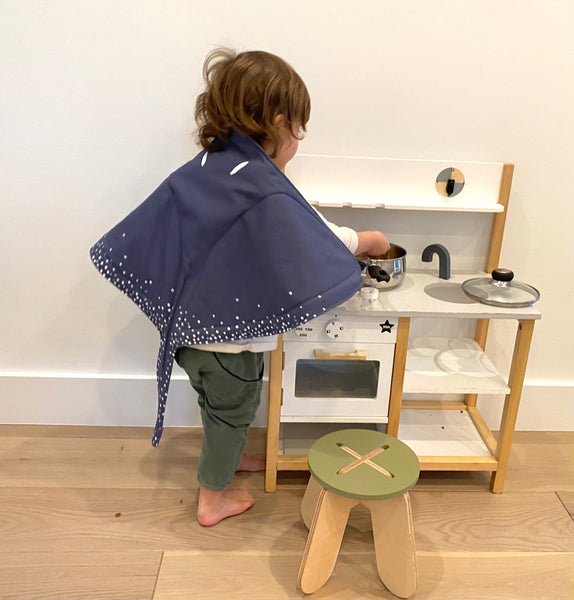Child playing dress up with play kitchen and stingray wings.