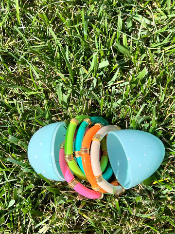 brightly colored resin bamboo stretch bracelets lay inside an easter egg in the grass on a sunny day