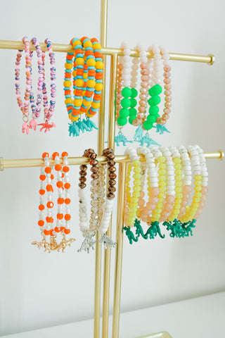 Six different dinosaur charm bracelets hang on a jewelry stand.