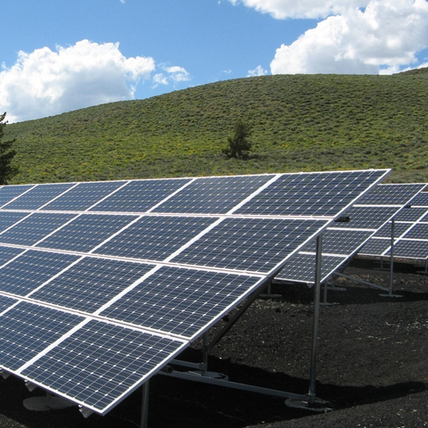 Image of solar panels on a grassy hill with a blue sky behind it