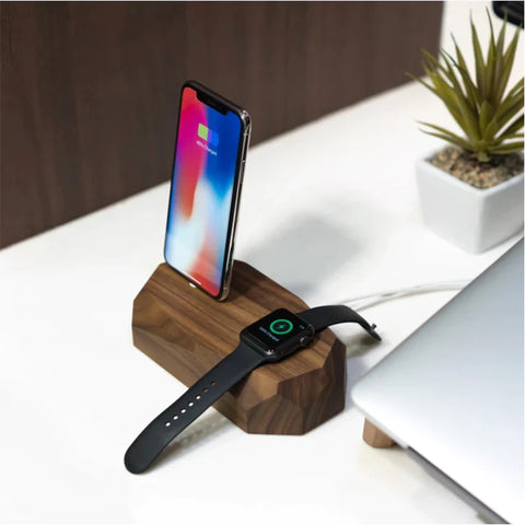 image of a white desk with a wooden phone and watch charger next to a laptop