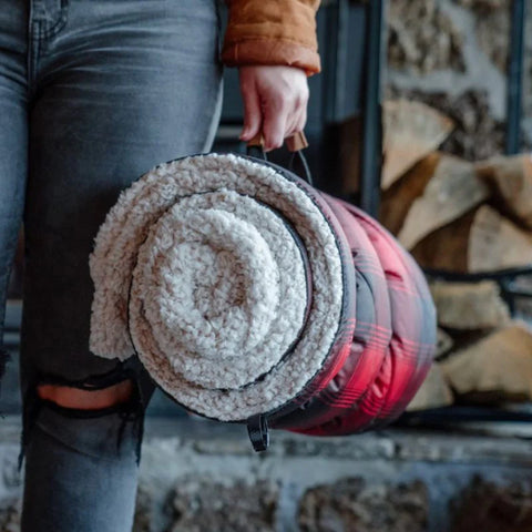 Image of person holding a rolled up Sherpa blanket standing in front of stacked wood