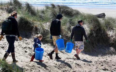 Image of 4 people carrying blue buckets walking on the beach toward the water.