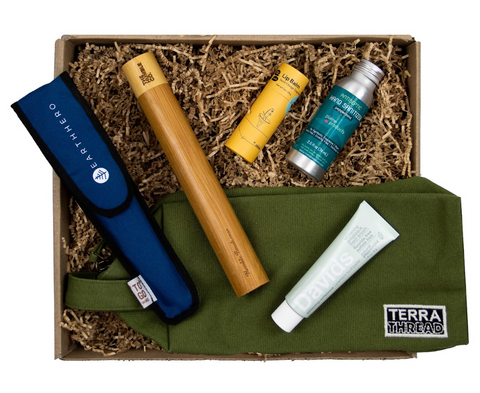 Image of a sustainable gift box that includes travel sized products like shampoo from Plain Products, lip balm from Meow Meow Tweet, a bamboo toothbrush travel case from Humble Col and a dopp kit from Terra Thread