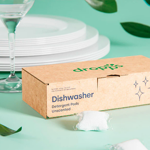 Image of a box of Dropps dishwasher pods on a green table with dinnerware and glasses