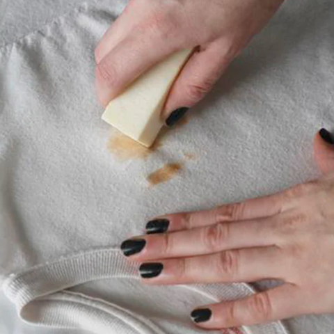 Image of a hand using a stain stick to remove a stain from a white tshirt