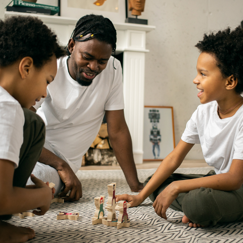 Image of a father and 2 young kids on the floor playing with toys