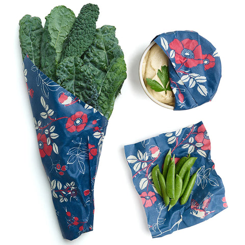 Image of dark blue Bees Wrap holding leafy greens, snap peas, and covering a bowl of hummus