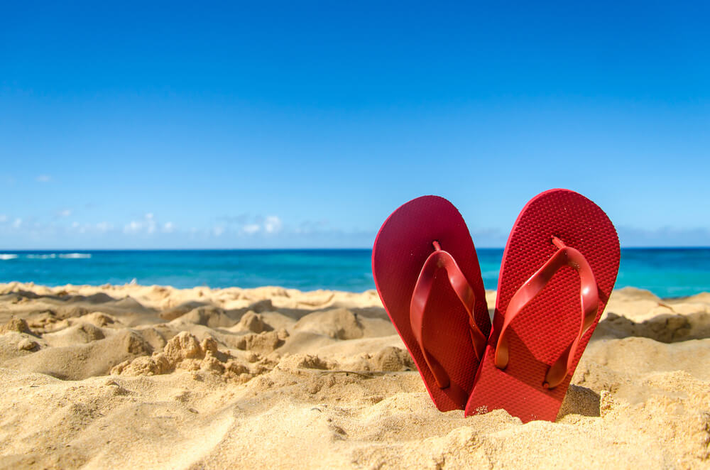 Pair of red flip flops pushed down on white sand on the beach.