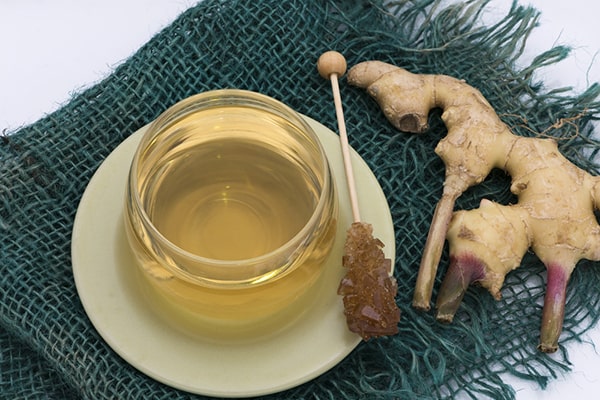 A woman with a bottle of ginger oil and a bowl of green tea - Uncover the synergistic Ginger Oil Benefits for Skin, Hair, and Aromatherapy in this enlightening post by MDBiowellness- Plant Medicine. Developed by Doctors.