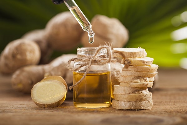 A woman with a bottle of ginger oil and a glass of water - Uncover the refreshing Ginger Oil Benefits for Skin, Hair, and Aromatherapy in this insightful post by MDBiowellness- Plant Medicine. Developed by Doctors.