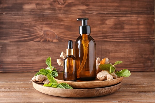 A woman with her hands in warm bath water infused with ginger oil - Uncover the rejuvenating Ginger Oil Benefits for Skin, Hair, and Aromatherapy in this enriching post by MDBiowellness- Plant Medicine. Developed by Doctors.