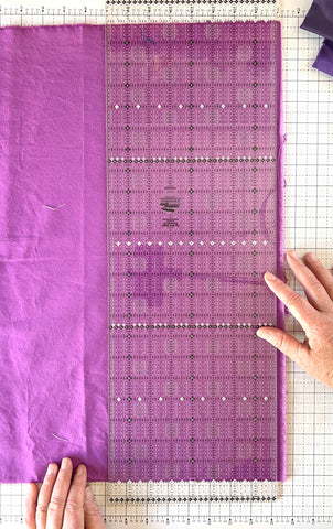 quilting ruler aligned with the straight edges of a purple piece of fabric