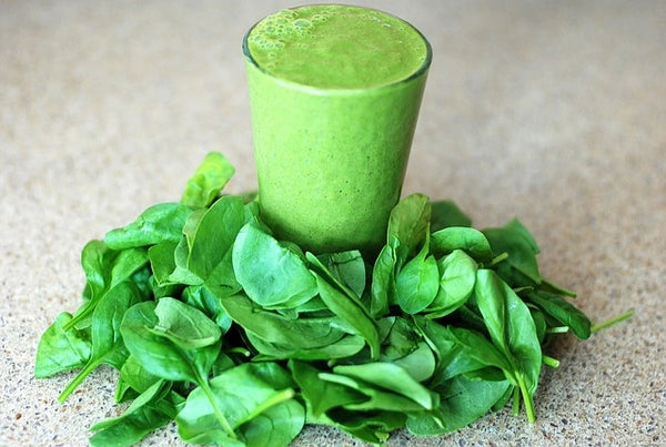 Smoothie vert vif dans un verre, posé sur un tas de feuilles d'épinards frais, évoquant une boisson saine riche en magnésium