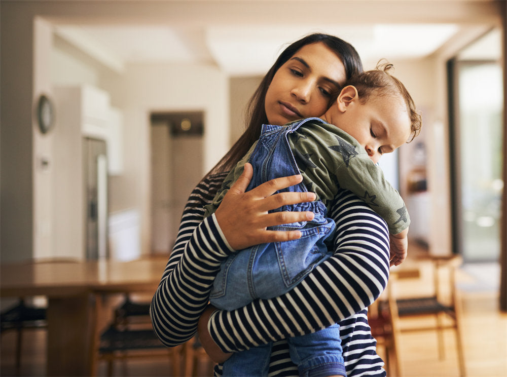 A young woman carrying her sleeping daughter through the living room