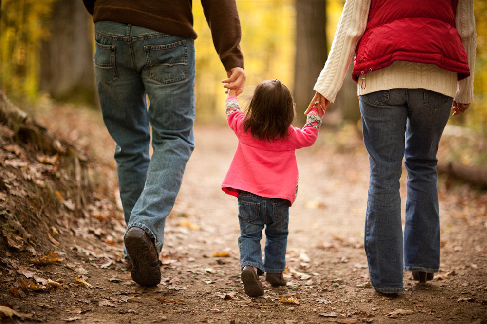 a family of three walking together on a trail through the woods outside during autumn