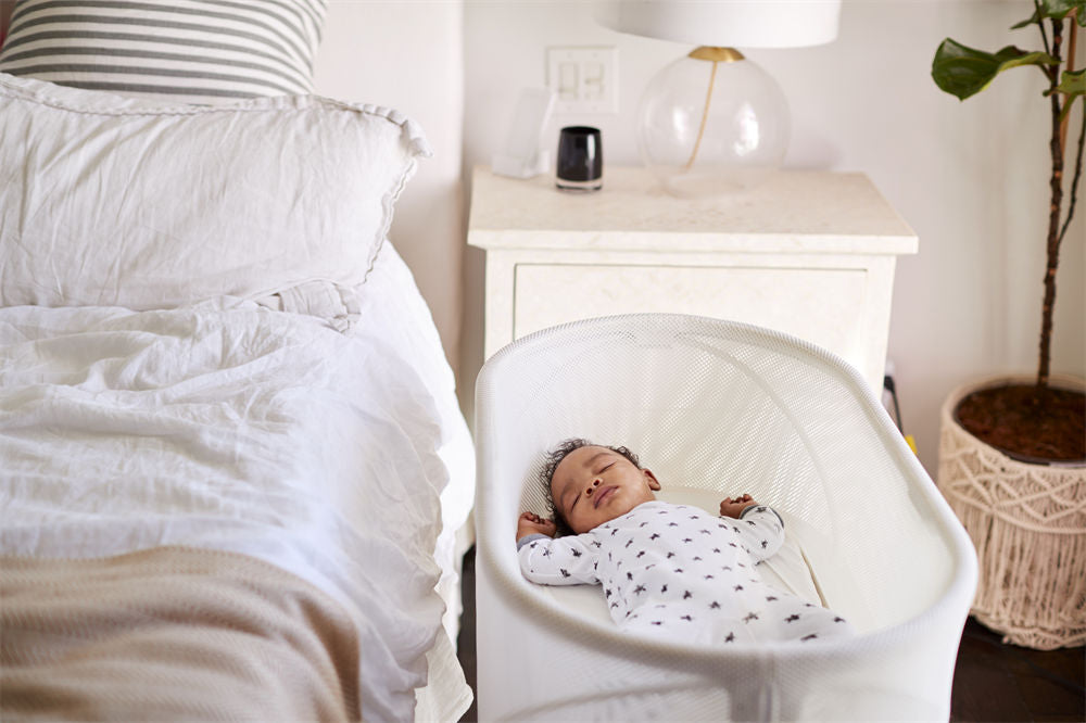 Three month old baby asleep in his cot beside the bed