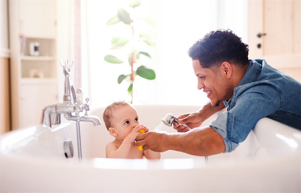 Father washing small toddler son in a bathroom indoors at home