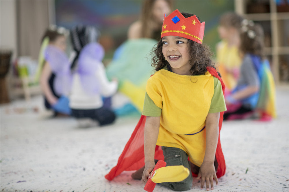 A boy with long hair of Indian descent smiles as he sticks out his sword that goes along with his king's costume