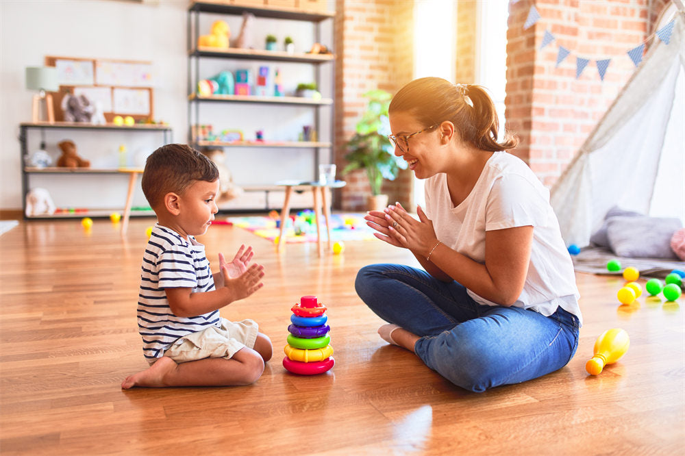 Beautiful teacher and toddler boy building pyramid with hoops bolcks at kindergarten