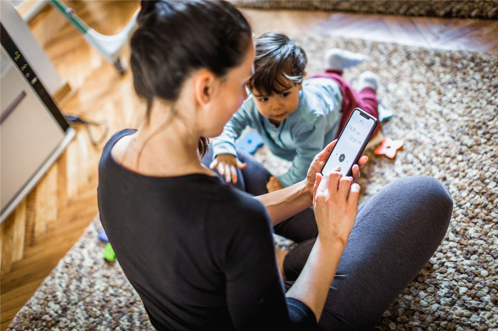 Woman exercising at home, using a mobile app while her baby boy interrupts