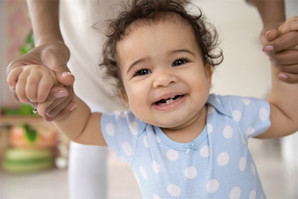 curly little toddler baby boy or girl with first teeth, learning making first steps with caring mother