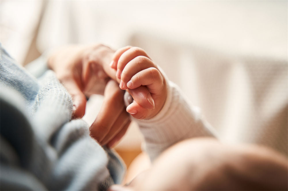 Close up view of the little newborn baby sleeping at the mother hands while holding her fingers with tender.