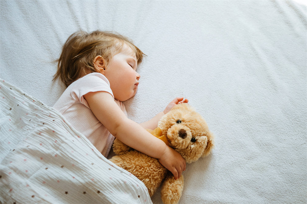 Little baby sleeping on bed embracing soft toy