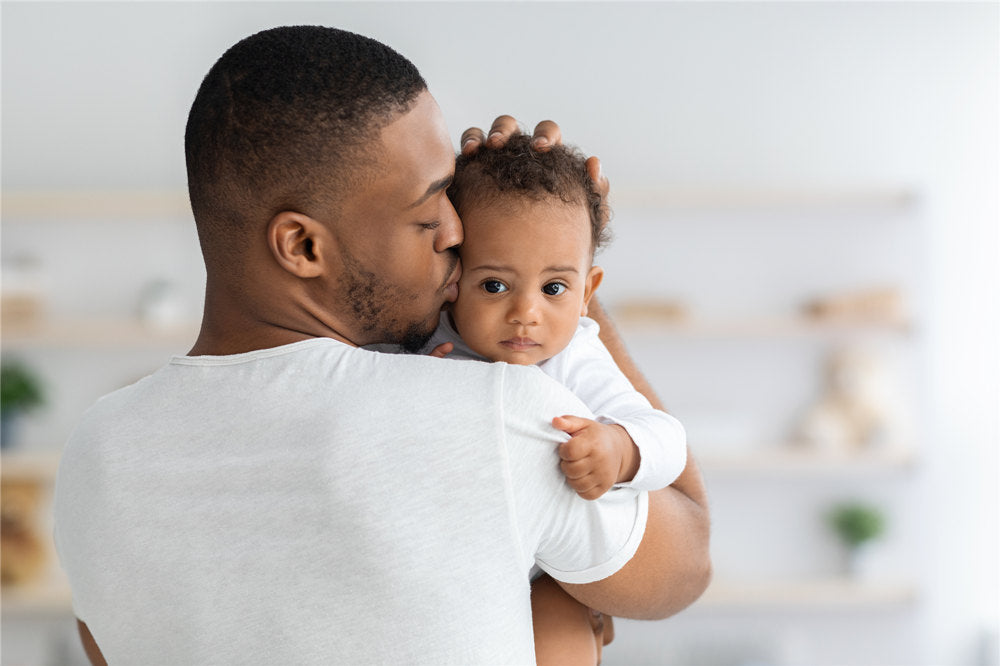 Father's Care. Young Black Dad Holding And Kissing Adorable Newborn Baby At Home