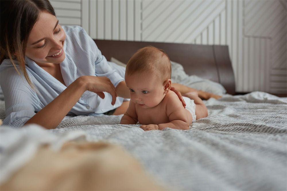 Portrait of young supportive mother and cute naked baby both lying in bed enjoying the moment together