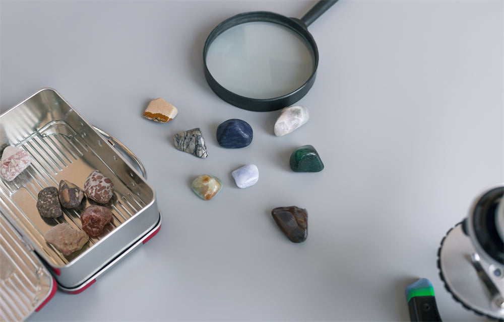 collection of semiprecious stones on gray table with magnifying glass, box and microscope