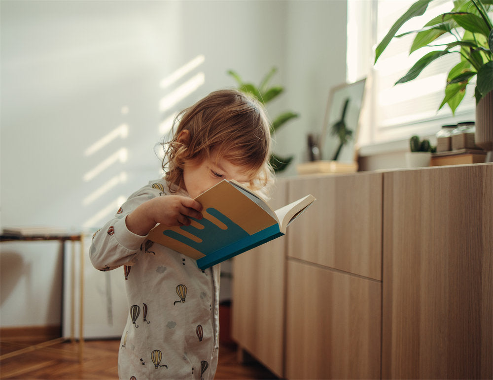 Cute baby girl is standing in her pyjamas holding and looking at the book