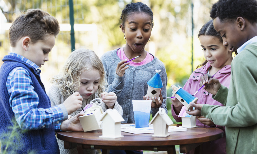 Multiracial children at community garden painting birdhouses